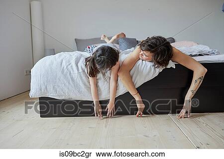Stock Photography - Mother and daughter lying on bed, hands touching floor. Fotosearch