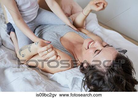 Stock Photo - Mother and daughter lying on bed, fooling around, laughing, mid section. Fotosearch