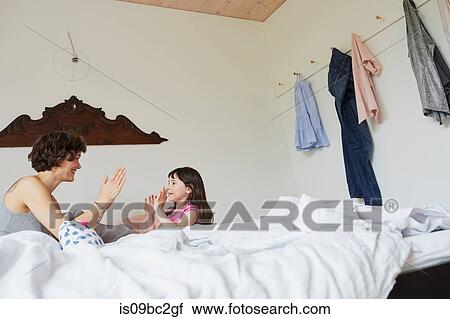 Stock Image - Mother and daughter playing in bedroom, smiling. Fotosearch
