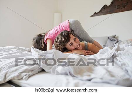 Stock Image - Mother and daughter playing on bed, daughter clambering over mother. Fotosearch