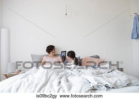 Mother and daughter relaxing in bed, daughter photographing mother using digital tablet View Large Photo Image Stock Photo - Mother and daughter relaxing in bed, daughter photographing mother using digital tablet. Fotosearch