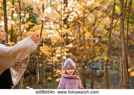 Picture - Mother and daughter throwing autumn leaves in air in forest. Fotosearch