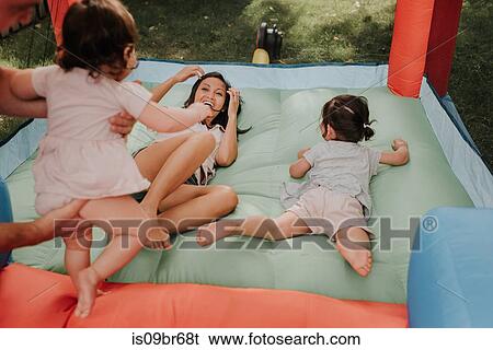 Stock Photograph - Mother and daughters playing on bouncy castle. Fotosearch