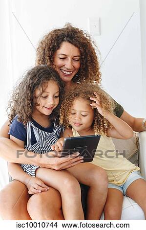 Picture - Mother and daughters using digital tablet at home. Fotosearch