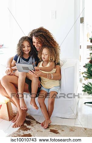 Stock Image - Mother and daughters using digital tablet at home. Fotosearch