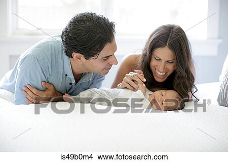 Picture - Mother and father leaning on bed, looking at newborn baby boy. Fotosearch