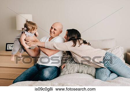 Mother and father on bed lifting up baby daughter View Large Photo Image Stock Image - Mother and father on bed lifting up baby daughter. Fotosearch