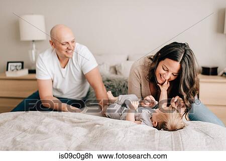 Stock Image - Mother and father on bed playing with baby daughter. Fotosearch