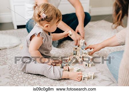 Mother and father on nursery floor with baby daughter playing with building blocks, cropped View Large Photo Image Picture - Mother and father on nursery floor with baby daughter playing with building blocks, cropped. Fotosearch