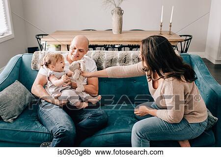 Mother and father on sofa with baby daughter playing with soft toy View Large Photo Image Stock Image - Mother and father on sofa with baby daughter playing with soft toy. Fotosearch