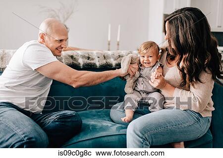 Mother and father on sofa with baby daughter playing with soft toy View Large Photo Image Stock Image - Mother and father on sofa with baby daughter playing with soft toy. Fotosearch