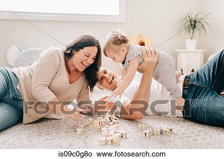 Mother and father reclining on nursery floor playing with baby daughter View Large Photo Image Picture - Mother and father reclining on nursery floor playing with baby daughter. Fotosearch