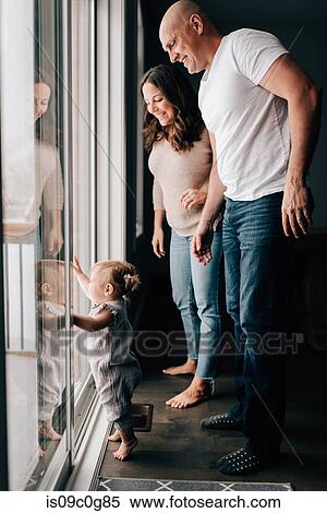 Stock Photography - Mother and father with baby daughter looking out through patio door. Fotosearch