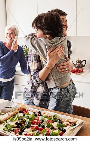 Mother and son hugging in kitchen, grandmother in background using smartphone View Large Photo Image Stock Image - Mother and son hugging in kitchen, grandmother in background using smartphone. Fotosearch