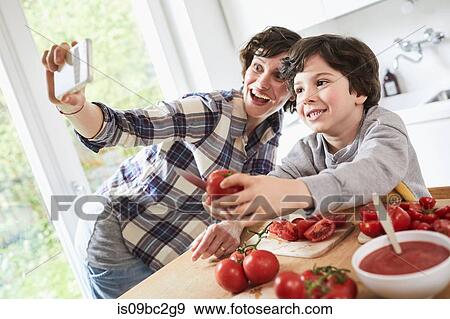 Mother and son preparing food in kitchen, mother taking selfie using smartphone View Large Photo Image Stock Photo - Mother and son preparing food in kitchen, mother taking selfie using smartphone. Fotosearch