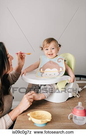 Mother feeding baby daughter in child seat, portrait View Large Photo Image Stock Photo - Mother feeding baby daughter in child seat, portrait. Fotosearch