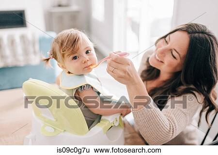 Mother feeding baby daughter in child seat, portrait View Large Photo Image Stock Photograph - Mother feeding baby daughter in child seat, portrait. Fotosearch