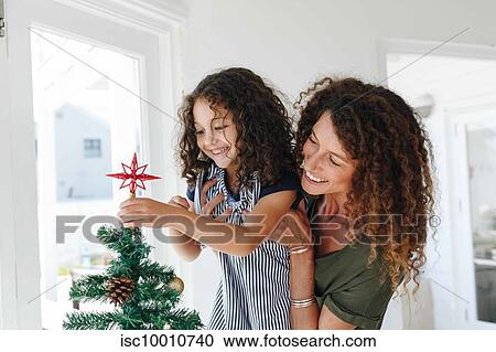Mother helping daughter place star on Christmas tree at home View Large Photo Image Stock Image - Mother helping daughter place star on Christmas tree at home. Fotosearch