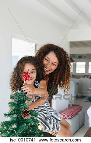 Mother helping daughter place star on Christmas tree at home View Large Photo Image Stock Image - Mother helping daughter place star on Christmas tree at home. Fotosearch