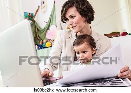 Mother holding sitting with baby daughter, working on laptop View Large Photo Image Stock Photo - Mother holding sitting with baby daughter, working on laptop. Fotosearch