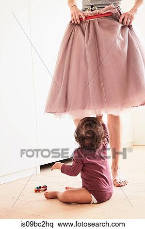 Mother holding skirt up against her, baby girl sitting on floor watching her, low section View Large Photo Image Stock Photography - Mother holding skirt up against her, baby girl sitting on floor watching her, low section. Fotosearch