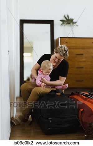 Stock Image - Mother on luggage with baby in bedroom. Fotosearch