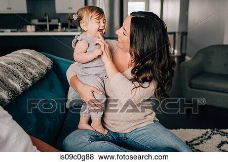 Stock Photo - Mother playing with baby daughter on sofa. Fotosearch