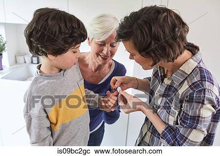 Stock Image - Mother putting plaster on son's finger, grandmother holding grandson's hand. Fotosearch