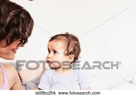 Stock Image - Mother sitting face to face with baby daughter, baby daughter with sad expression. Fotosearch