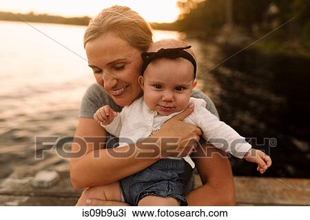 Mother sitting on pier hugging baby daughter View Large Photo Image Stock Image - Mother sitting on pier hugging baby daughter. Fotosearch