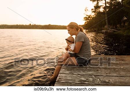 Mother sitting on pier with baby daughter looking down at lake View Large Photo Image Stock Image - Mother sitting on pier with baby daughter looking down at lake. Fotosearch