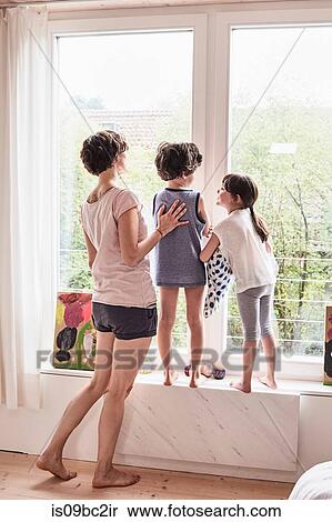 Stock Photography - Mother, son and daughter at home, looking out of window, rear view. Fotosearch