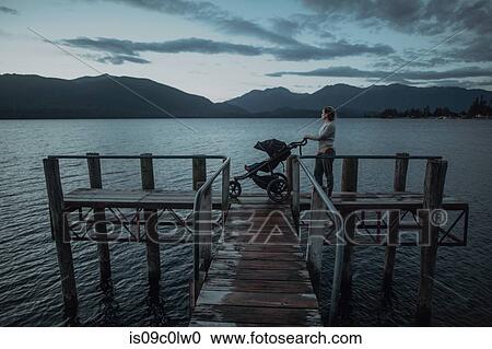 Stock Image - Mother with baby in pram on bridge by seaside, Te Anau, Southland, New Zealand. Fotosearch