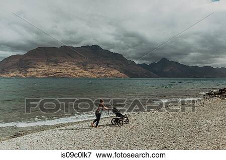 Stock Photo - Mother with baby in pram walking on beach, Queenstown, Canterbury, New Zealand. Fotosearch