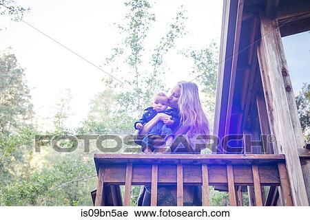 Mother with baby son on balcony of wooden house in forest, Cazadero, California, USA View Large Photo Image Stock Image - Mother with baby son on balcony of wooden house in forest, Cazadero, California, USA. Fotosearch