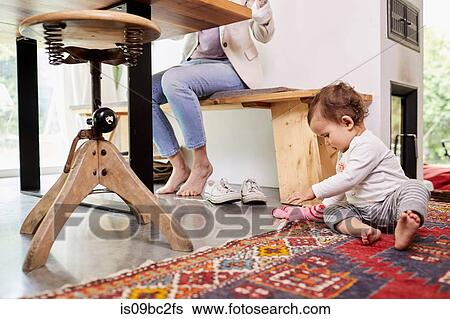 Stock Photograph - Mother working at kitchen table, whilst baby girl plays on floor. low section. Fotosearch