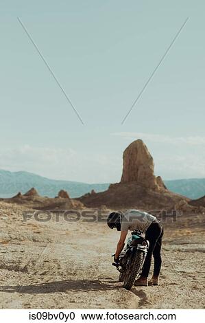 Stock Image - Motorcyclist bending over bike in desert, Trona Pinnacles, California, US. Fotosearch
