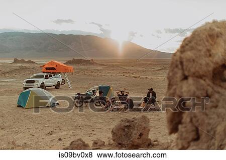 Stock Photo - Motorcyclist road trippers around camp fire, Trona Pinnacles, California, US. Fotosearch