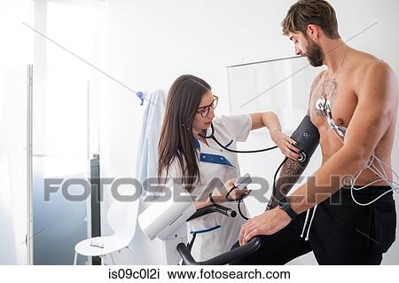 Stock Image - Nurse performing ECG test on patient in consultation room. Fotosearch