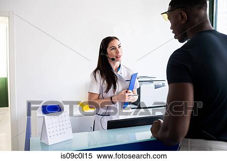 Stock Photography - Nurse speaking with patient at hospital reception. Fotosearch