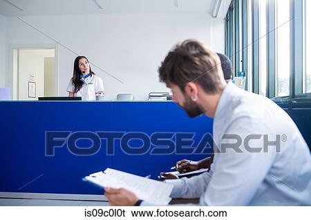 Nurse speaking with patients completing forms at hospital reception View Large Photo Image Stock Photograph - Nurse speaking with patients completing forms at hospital reception. Fotosearch