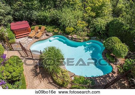 Stock Image - Outdoor swimming pool surrounded by wrought iron security fence and various shrubs and trees in luxury residential backyard, high angle view. Fotosearch