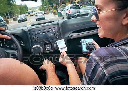 Stock Image - Over shoulder view of road trip couple driving and holding instant photograph, Breckenridge, Colorado, USA. Fotosearch