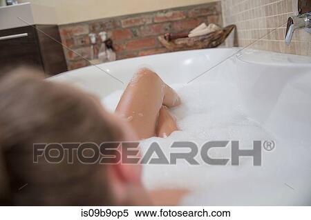 Stock Photography - Over shoulder view of young woman reclining in bubble bath. Fotosearch