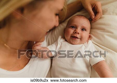 Stock Photo - Overhead portrait of woman and baby daughter lying on bed. Fotosearch