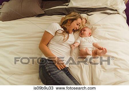 Stock Image - Overhead view of woman and baby daughter lying on bed. Fotosearch