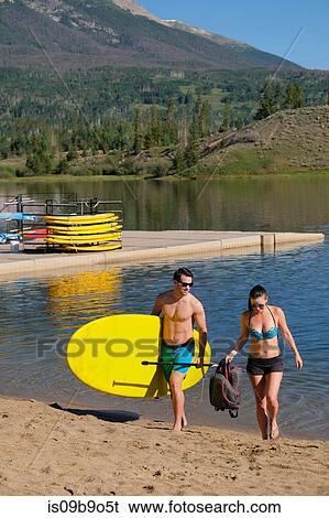 Stock Photograph - Paddleboarding couple carrying paddleboard on lake shore, Frisco, Colorado, USA. Fotosearch