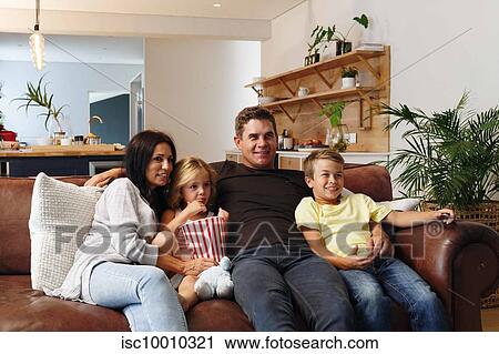 Stock Image - Parents and children relaxing with popcorn on sofa at home. Fotosearch
