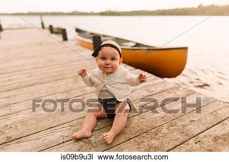 Stock Image - Portrait of baby girl sitting on lake pier. Fotosearch