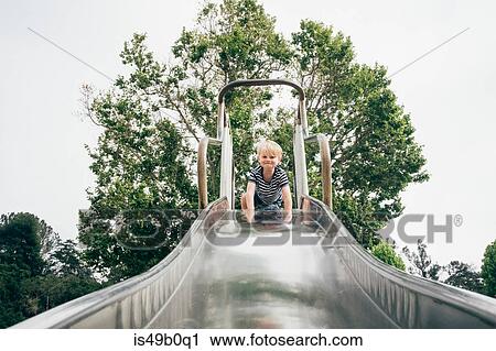 Stock Image - Portrait of boy at top of playground slide, low angle view. Fotosearch